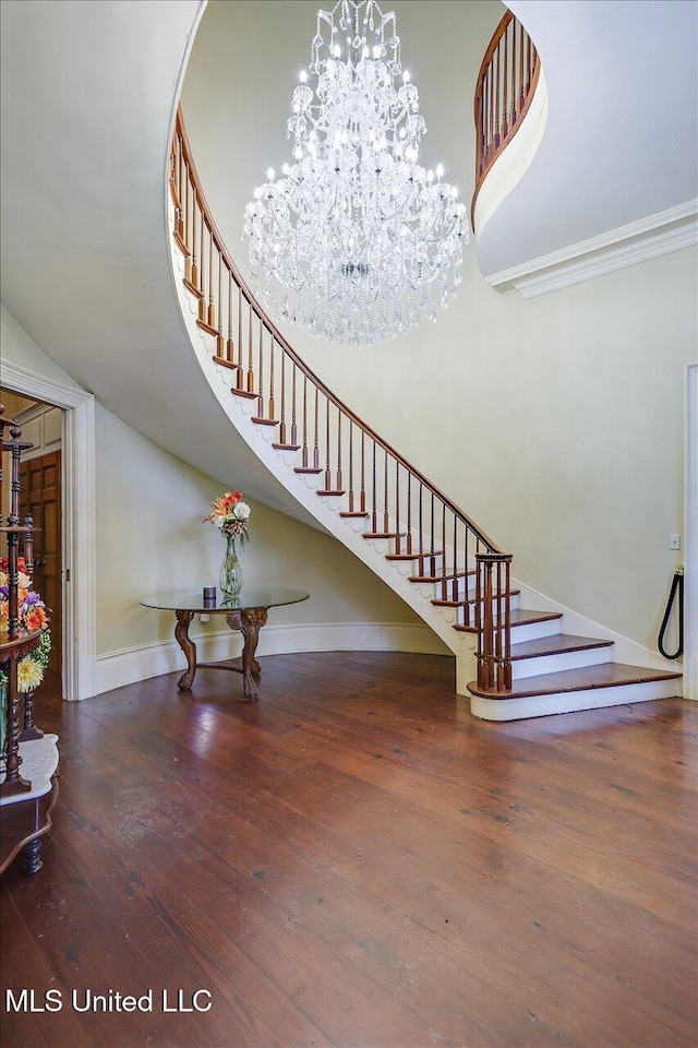 stairs with a notable chandelier, wood-type flooring, ornamental molding, and a towering ceiling