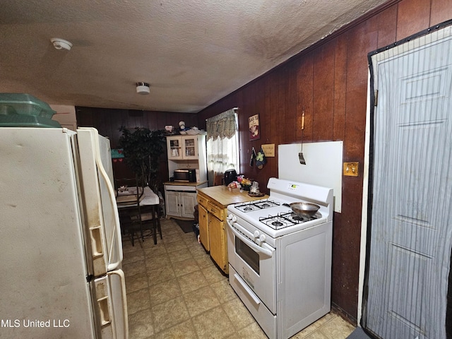 kitchen with white appliances, wood walls, and a textured ceiling