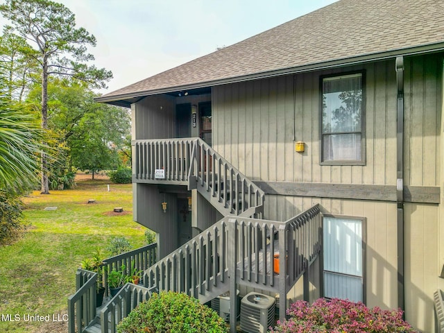 property entrance with central AC unit, a lawn, and roof with shingles