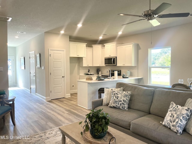 living room featuring ceiling fan, sink, and light wood-type flooring