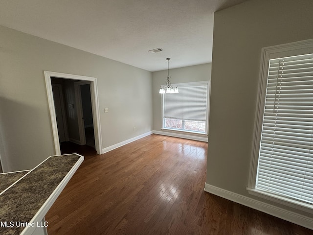 unfurnished dining area featuring an inviting chandelier and dark hardwood / wood-style flooring