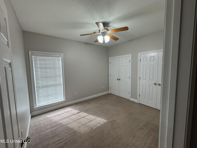 unfurnished bedroom with ceiling fan, a textured ceiling, light colored carpet, and multiple closets