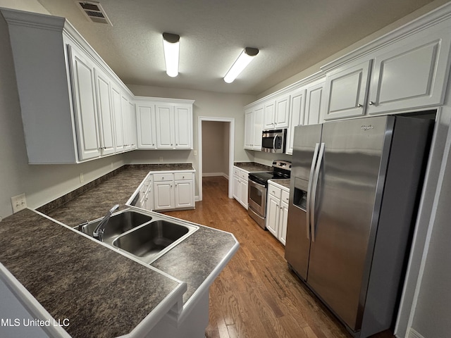 kitchen with dark hardwood / wood-style floors, sink, white cabinets, kitchen peninsula, and stainless steel appliances