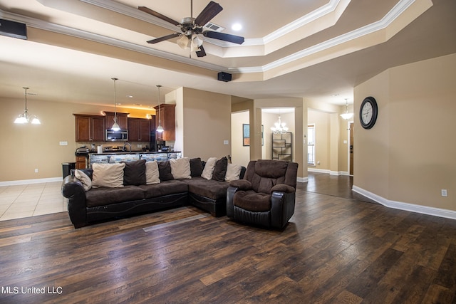 living room featuring ornamental molding, dark hardwood / wood-style floors, ceiling fan with notable chandelier, and a raised ceiling