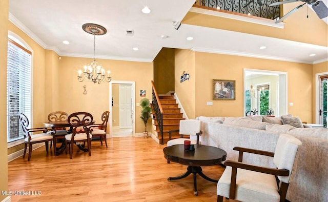 living room with ornamental molding, ceiling fan with notable chandelier, and light wood-type flooring