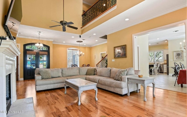 living room featuring crown molding, light hardwood / wood-style floors, a towering ceiling, a premium fireplace, and ceiling fan with notable chandelier