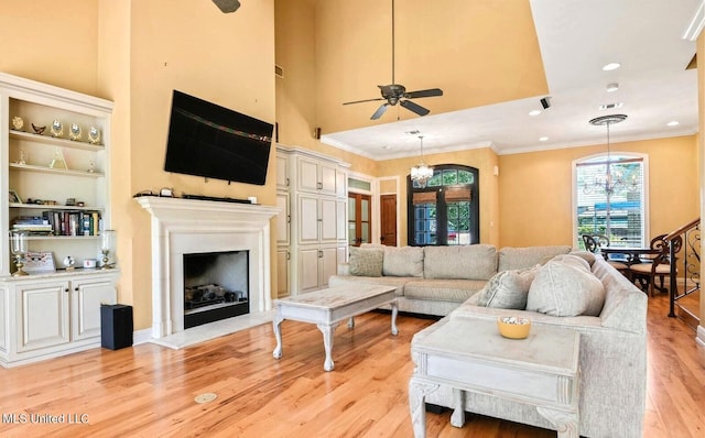 living room with a high ceiling, ornamental molding, ceiling fan with notable chandelier, french doors, and light wood-type flooring