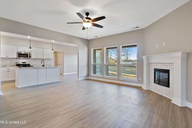 unfurnished living room with sink, a fireplace, light wood-type flooring, and ceiling fan