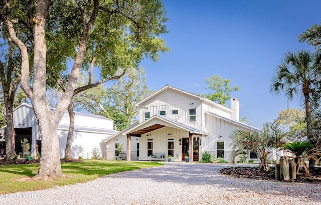 modern farmhouse style home featuring board and batten siding, gravel driveway, a chimney, and a front lawn