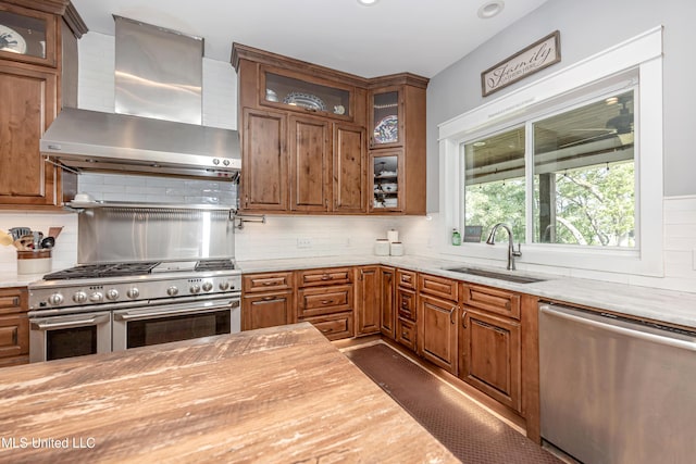 kitchen with wall chimney range hood, stainless steel appliances, a sink, and backsplash