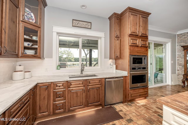 kitchen with light stone countertops, a sink, brick floor, stainless steel appliances, and decorative backsplash