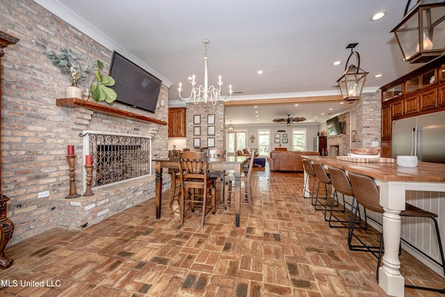 dining space featuring ceiling fan with notable chandelier, a brick fireplace, brick floor, and ornamental molding