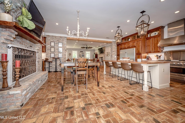 kitchen with wall chimney exhaust hood, brick floor, high end appliances, and brown cabinets
