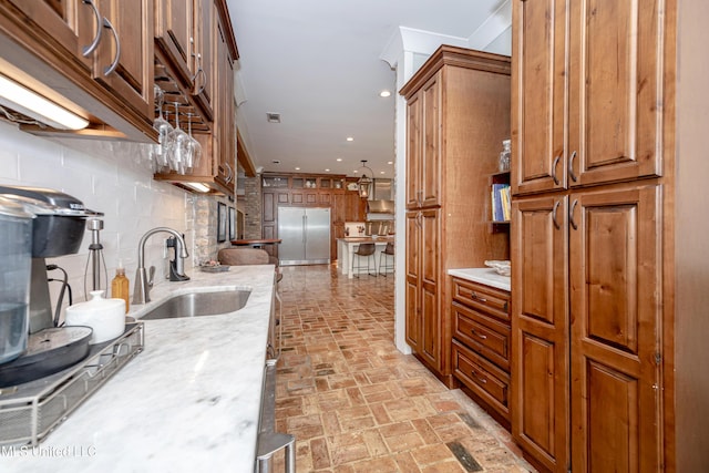kitchen with brown cabinets, a sink, brick floor, decorative backsplash, and built in refrigerator