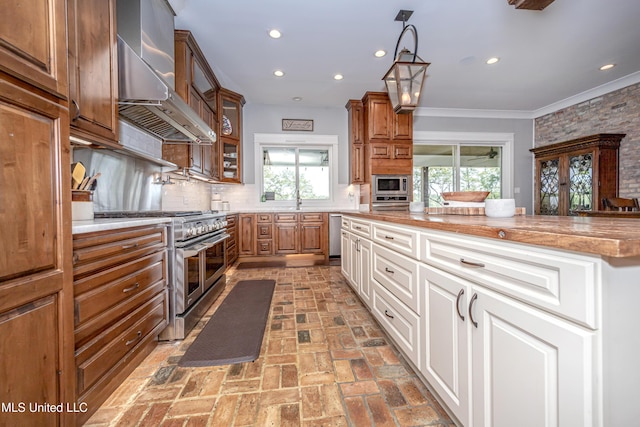 kitchen featuring brown cabinets, appliances with stainless steel finishes, a healthy amount of sunlight, and wall chimney exhaust hood