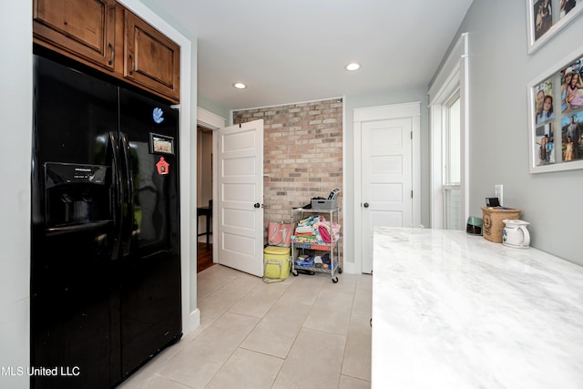 kitchen featuring black fridge, brick wall, brown cabinetry, recessed lighting, and light tile patterned floors
