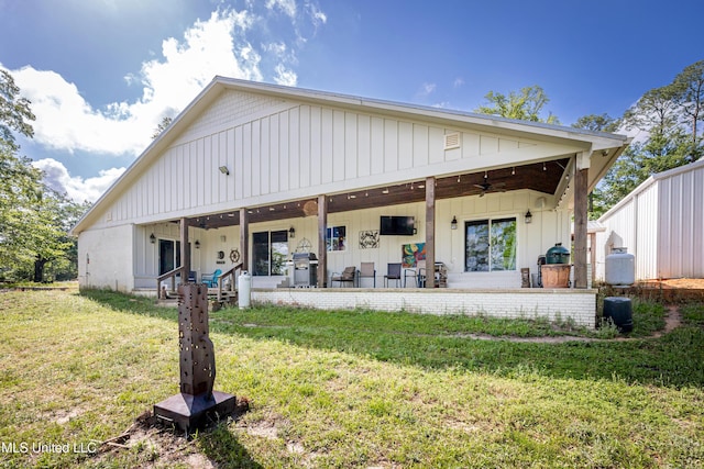 rear view of property featuring a ceiling fan, board and batten siding, a patio area, and a yard