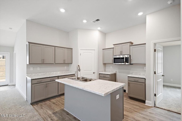 kitchen featuring gray cabinets, light hardwood / wood-style flooring, sink, and an island with sink