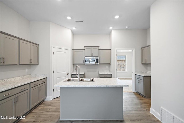 kitchen featuring a center island with sink, gray cabinetry, and wood-type flooring