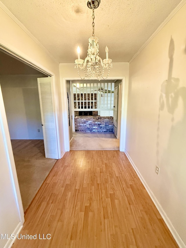 corridor with a textured ceiling, hardwood / wood-style flooring, an inviting chandelier, and ornamental molding