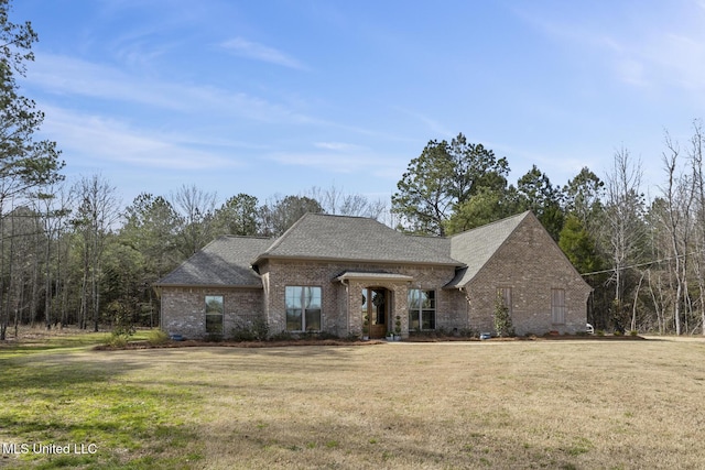 view of front of property with a shingled roof, a front lawn, and brick siding