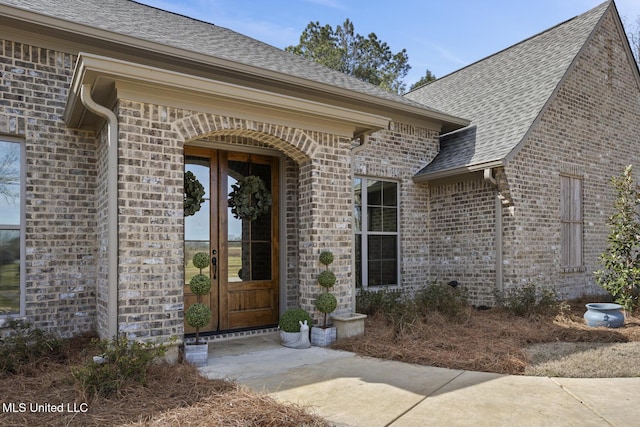 view of exterior entry featuring brick siding, a shingled roof, and french doors