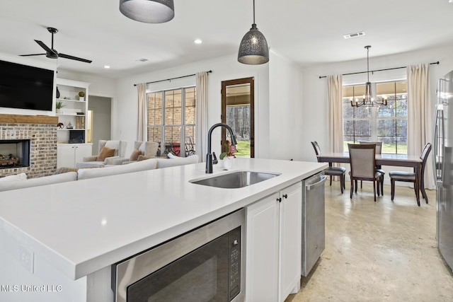 kitchen with visible vents, appliances with stainless steel finishes, a kitchen island with sink, a fireplace, and a sink