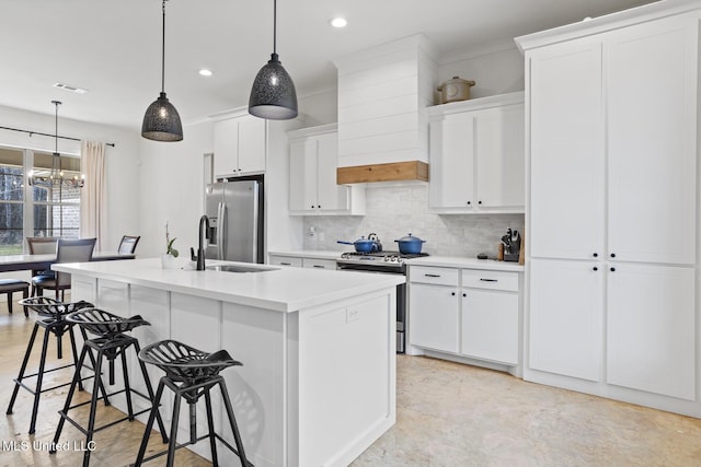 kitchen with stainless steel appliances, tasteful backsplash, white cabinetry, a kitchen island with sink, and a kitchen breakfast bar