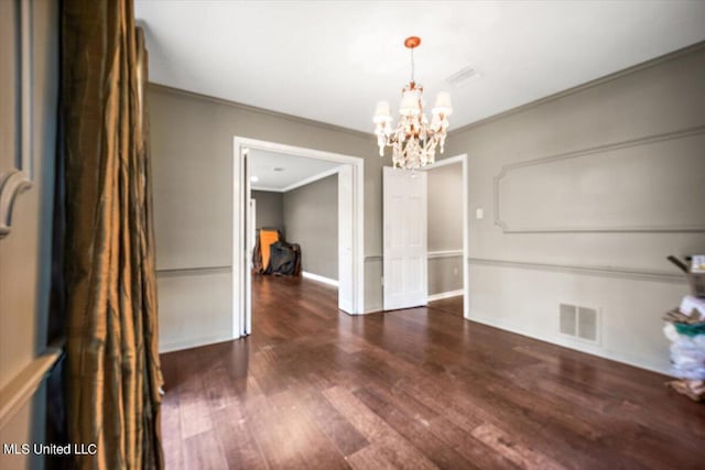 spare room featuring ornamental molding, a chandelier, and dark wood-type flooring