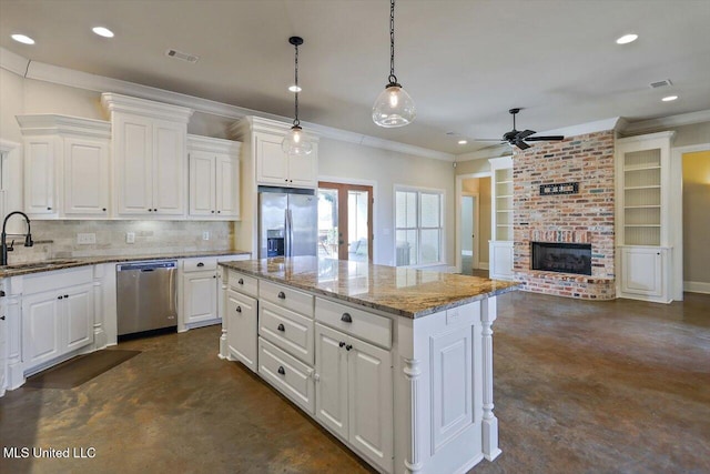 kitchen with sink, appliances with stainless steel finishes, white cabinetry, a kitchen island, and decorative light fixtures