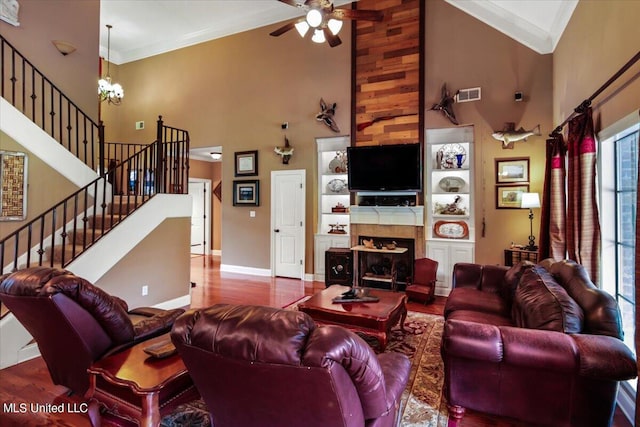 living room with hardwood / wood-style floors, ornamental molding, ceiling fan with notable chandelier, a towering ceiling, and wooden walls