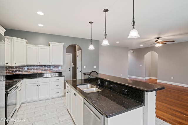 kitchen with arched walkways, a sink, appliances with stainless steel finishes, backsplash, and an island with sink