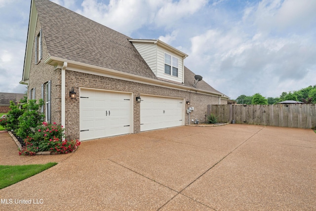 view of side of home featuring a garage, brick siding, roof with shingles, and fence