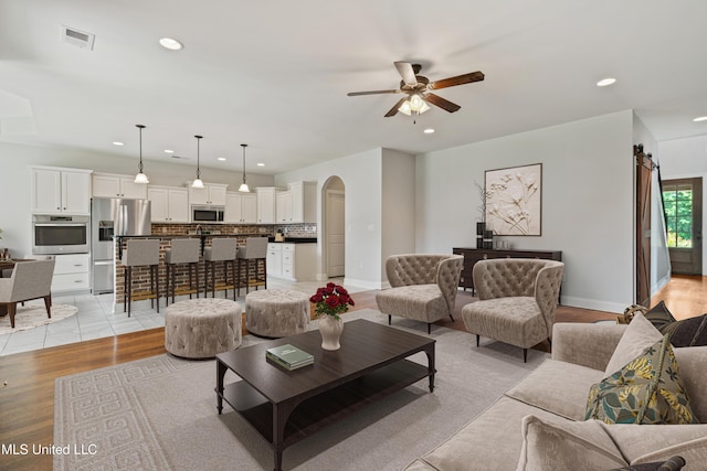 living area with a barn door, arched walkways, a ceiling fan, light wood-style flooring, and recessed lighting