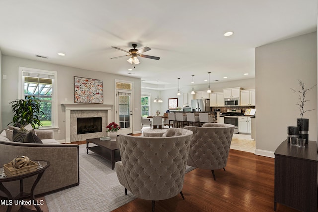 living area featuring recessed lighting, light wood-style flooring, a tiled fireplace, ceiling fan, and baseboards