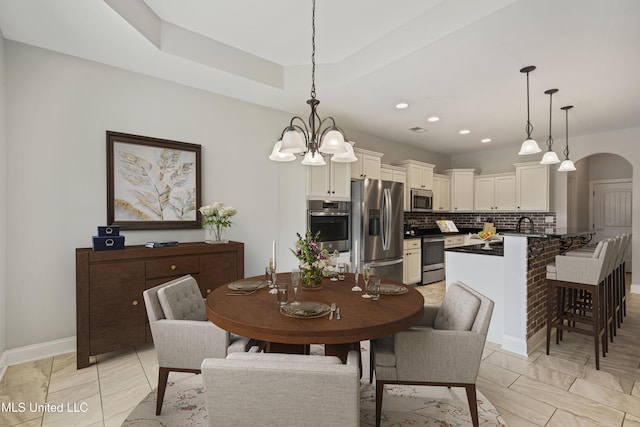 dining room with arched walkways, recessed lighting, a raised ceiling, and baseboards