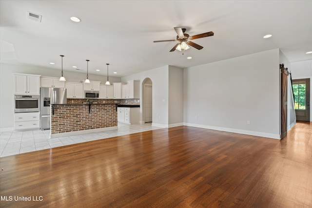 unfurnished living room featuring arched walkways, visible vents, a barn door, a ceiling fan, and light wood-type flooring