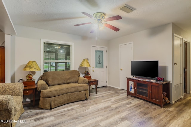 living room with baseboards, light wood-style flooring, a textured ceiling, visible vents, and ceiling fan