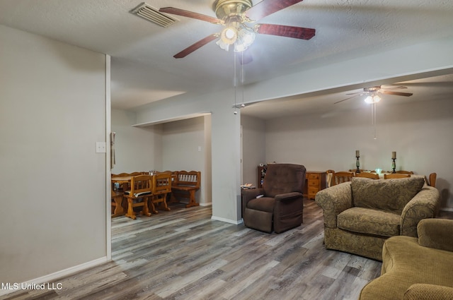 living room featuring visible vents, baseboards, a ceiling fan, and wood finished floors