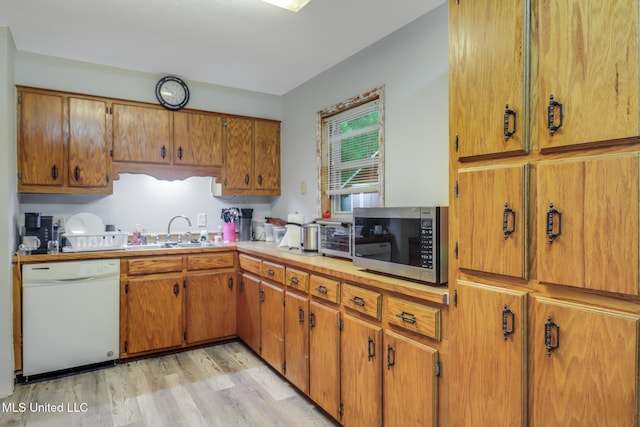 kitchen featuring stainless steel microwave, light wood-type flooring, brown cabinetry, white dishwasher, and a sink