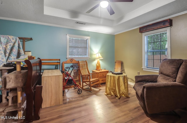 sitting room with crown molding, a ceiling fan, visible vents, a raised ceiling, and wood finished floors