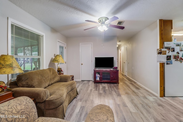 living room featuring visible vents, baseboards, a ceiling fan, a textured ceiling, and light wood-style flooring