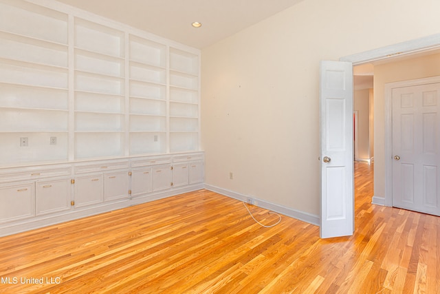 unfurnished room featuring built in shelves and light hardwood / wood-style floors