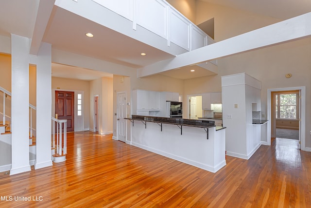 kitchen with a towering ceiling, kitchen peninsula, a breakfast bar area, white cabinets, and light hardwood / wood-style flooring