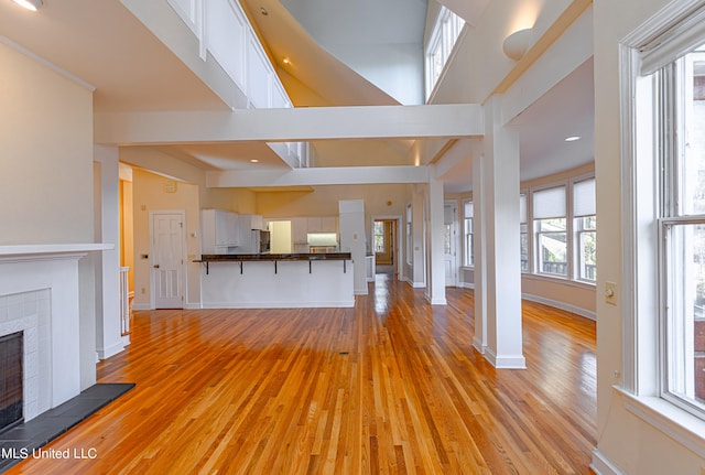 unfurnished living room with a towering ceiling, light wood-type flooring, and a fireplace