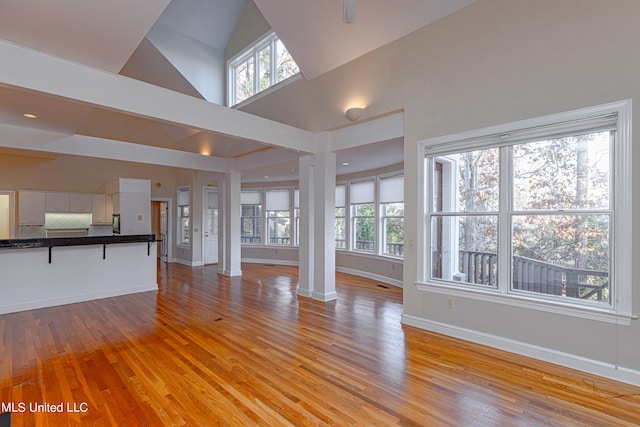 unfurnished living room with decorative columns, high vaulted ceiling, and light wood-type flooring