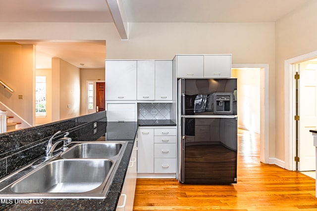 kitchen featuring decorative backsplash, white cabinetry, light wood-type flooring, dark stone countertops, and sink