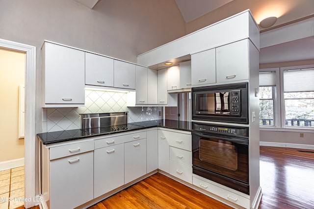 kitchen with white cabinetry, tasteful backsplash, black appliances, and light hardwood / wood-style flooring