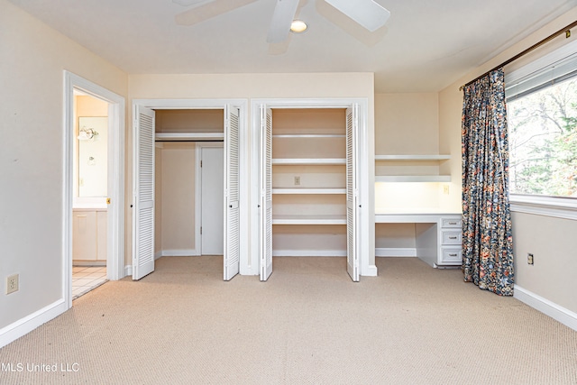 unfurnished bedroom featuring built in desk, two closets, light colored carpet, and ceiling fan