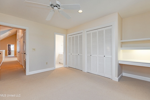 unfurnished bedroom featuring light carpet, lofted ceiling, multiple closets, and ceiling fan